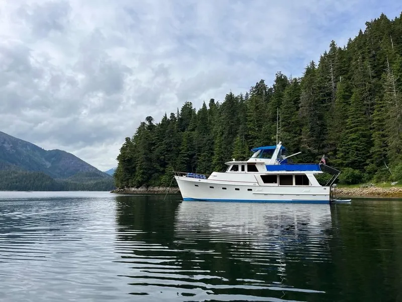 The Image of 1980 Ocean Alexander 50 MK1 yacht on calm water, surrounded by lush forest and mountains. - 0