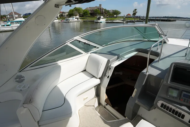 Slide: The Image of 2005 CRUISERS YACHT 340 Express interior with white seating, docked by a serene waterfront. - 9