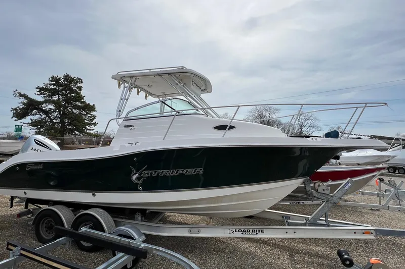Slide: The Image of 2006 Striper 2301 Walkaround OB boat on trailer, parked outdoors under cloudy sky. - 10