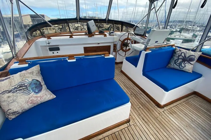 Slide: The Image of 1980 CHB Trawler interior with blue seating, nautical-themed pillows, and wooden steering wheel. - 8