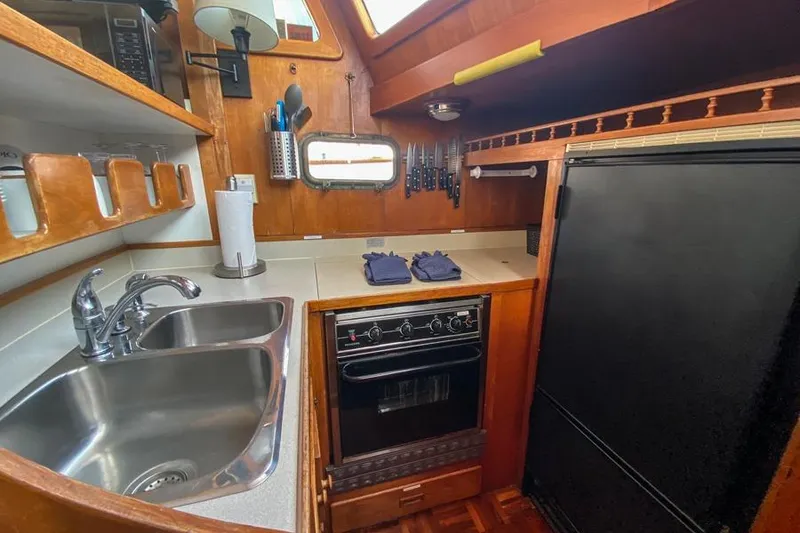 Slide: The Image of 1980 CHB Trawler kitchen with sink, stove, and refrigerator in a wooden interior. - 9