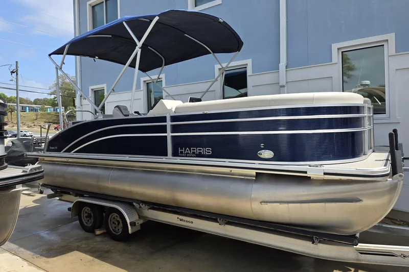 Slide: The Image of 2021 Harris Cruiser 230 pontoon boat on trailer, blue and white design, parked outdoors. - 6