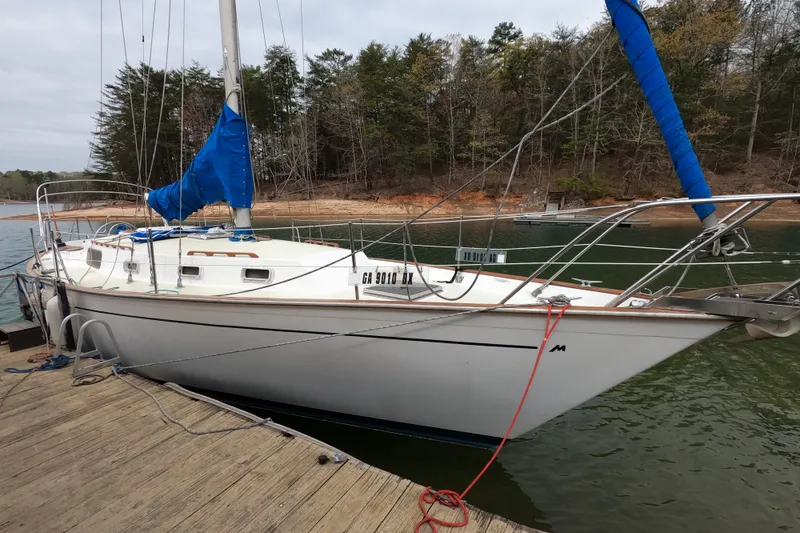 The Image of 1980 Morgan 382 sailboat docked on a serene lake with forested shoreline. - 0