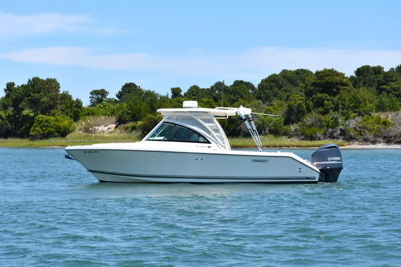 The Image of 2012 Pursuit DC 265 Dual Console boat on calm water near a wooded shoreline. - 0