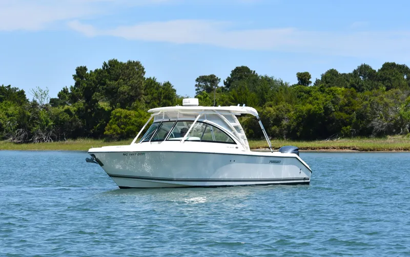 Slide: The Image of 2012 Pursuit DC 265 Dual Console boat on calm water, surrounded by lush greenery. - 2