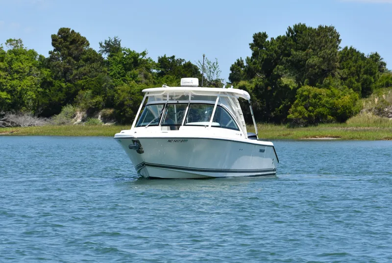 Slide: The Image of 2012 Pursuit DC 265 Dual Console boat on calm water, surrounded by lush greenery. - 3