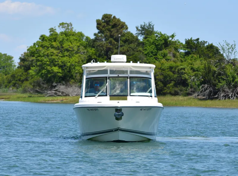 Slide: The Image of 2012 Pursuit DC 265 Dual Console boat cruising on a calm lake with lush greenery. - 4