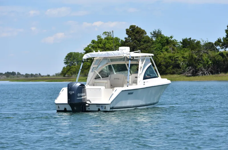 Slide: The Image of 2012 Pursuit DC 265 Dual Console boat on calm water near a green shoreline. - 7