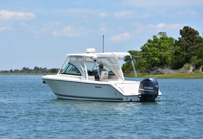 Slide: The Image of 2012 Pursuit DC 265 Dual Console boat on calm water near a green shoreline. - 9