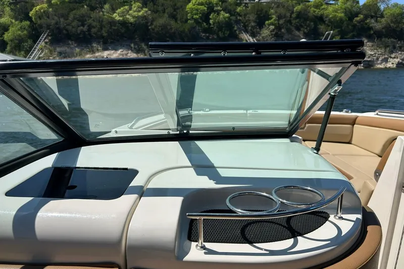 Slide: The Image of 2015 Sea Ray 270 Sundeck interior with cup holders and open windshield, near scenic water. - 39
