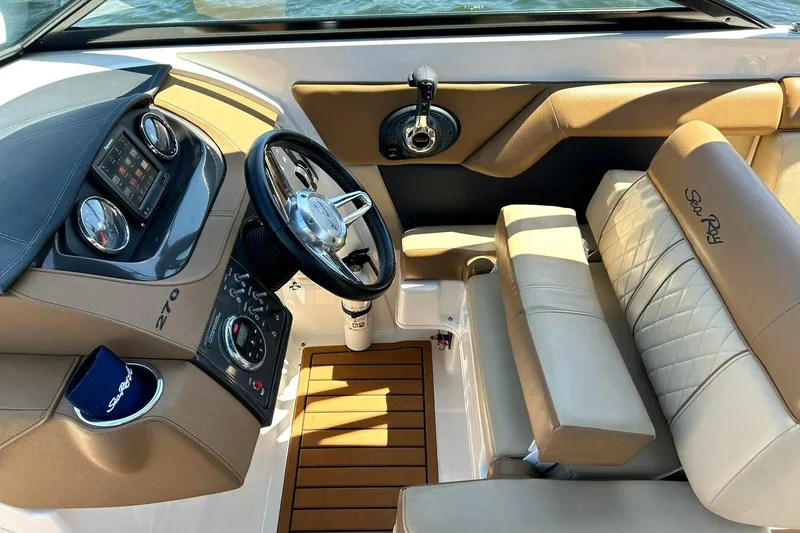 Slide: The Image of 2015 Sea Ray 270 Sundeck cockpit with steering wheel, dashboard, and beige seating. - 45