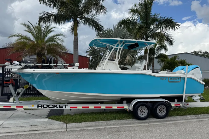 The Image of 2024 Key West 263 FS boat on trailer, vibrant blue, parked near palm trees. - 1