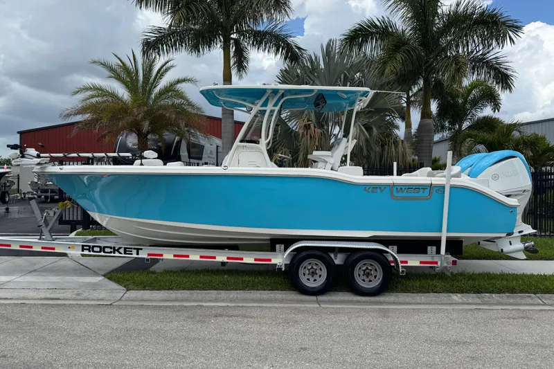 Slide: The Image of 2024 Key West 263 FS boat on trailer, vibrant blue, parked near palm trees. - 2