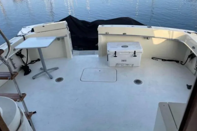 Slide: The Image of 1978 Hatteras 45 Express Sportfish boat deck with table and cooler, docked by calm water. - 7