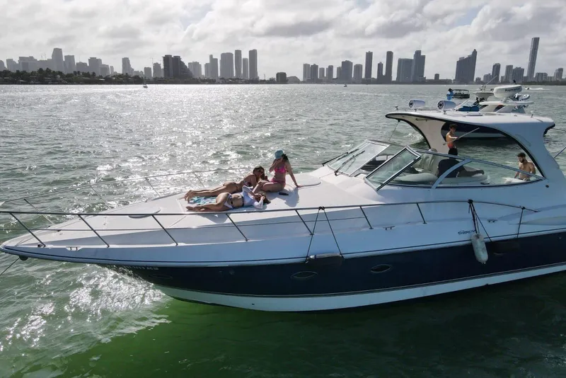 Slide: The Image of 2005 Cruisers Yachts 440 Express on water with people relaxing, city skyline in background. - 2