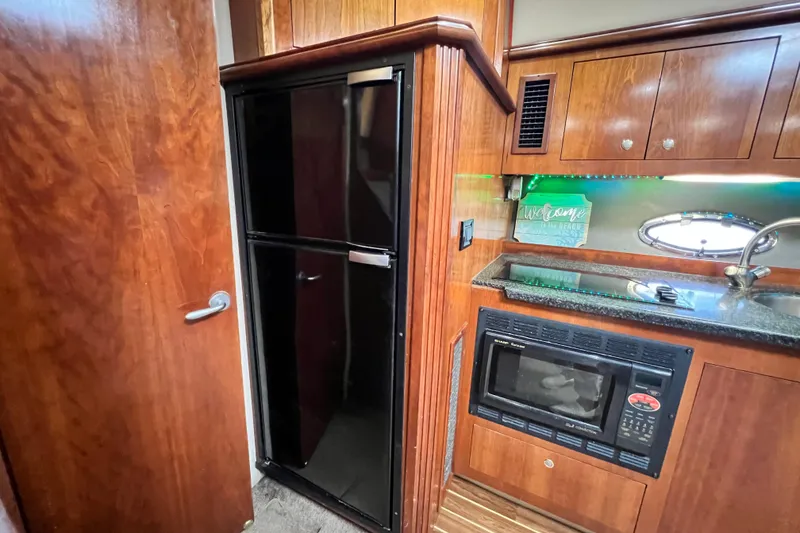 Slide: The Image of 2005 Cruisers Yachts 440 Express kitchen with wood cabinetry, black fridge, and microwave. - 59
