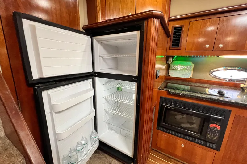 Slide: The Image of 2005 Cruisers Yachts 440 Express kitchen with open fridge, microwave, and wooden cabinetry. - 60