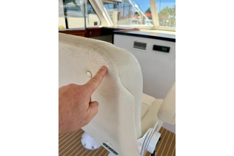 Slide: The Image of Close-up of a hand pointing at cracked upholstery on a 2006 Huckins Atlantic 44 boat seat. - 22