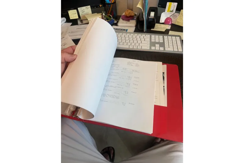 Slide: The Image of Person reviewing documents in a red folder on a desk with a keyboard. - 53