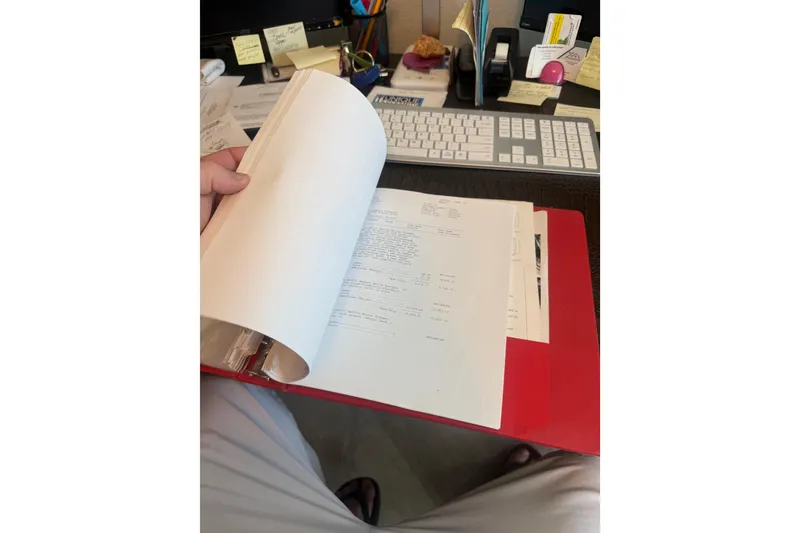 Slide: The Image of Person reviewing documents in a red folder at a cluttered desk. - 54