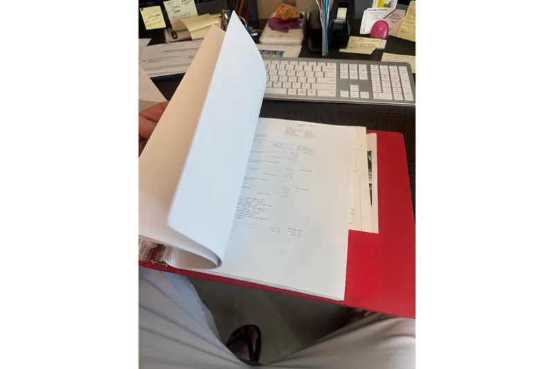 Slide: The Image of Person reviewing documents in a red folder at a desk with a keyboard. - 75