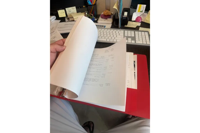 Slide: The Image of Person reviewing documents at a desk with a red folder, Huckins Atlantic 44, 2006. - 77