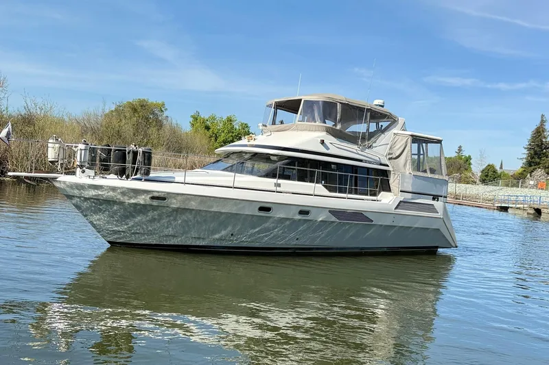 Slide: The Image of 1991 Bayliner 4387 Motoryacht on calm water, surrounded by greenery and clear blue sky. - 2