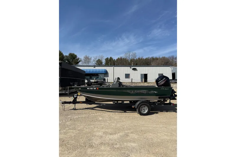 The Image of 2017 Lund 1775 Impact SS boat on trailer, parked outdoors near industrial building. - 0