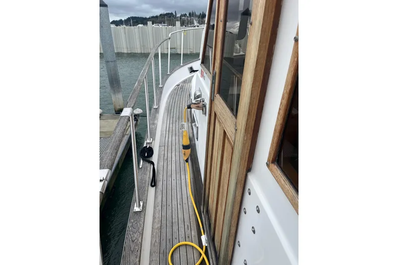 Slide: The Image of 1986 Sea Ranger 47 Pilothouse yacht docked, showcasing wooden deck and cabin door. - 19