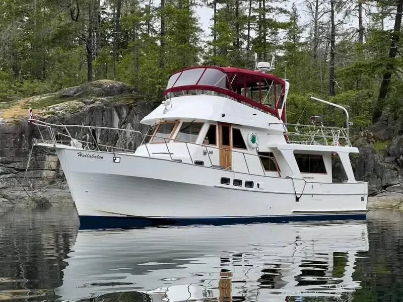 Slide: The Image of 1986 Sea Ranger 47 Pilothouse yacht anchored near rocky shoreline with trees. - 2