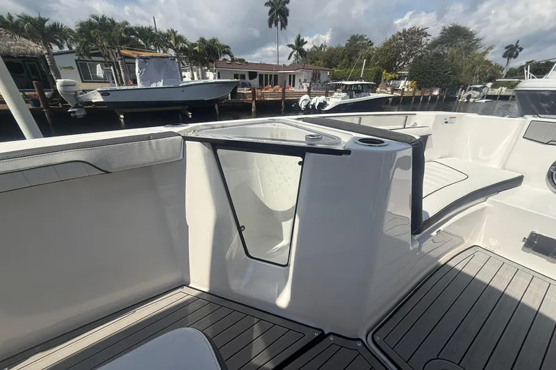 Slide: The Image of 2024 Yamaha Boats 255 FSH Sport H interior with seating and storage, docked near palm trees. - 16