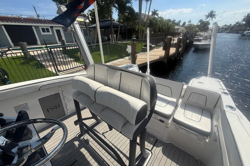 Slide: The Image of 2024 Yamaha Boats 255 FSH Sport H interior with seating and steering wheel, docked by a canal. - 19