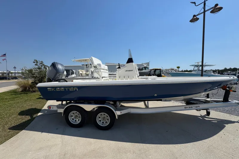 Slide: The Image of 2025 Skeeter SX221 boat on trailer, parked outdoors under clear blue sky. - 2