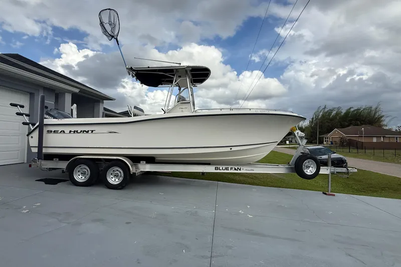 Slide: The Image of 2005 Sea Hunt Triton 232 boat on trailer, parked beside a garage under cloudy sky. - 2
