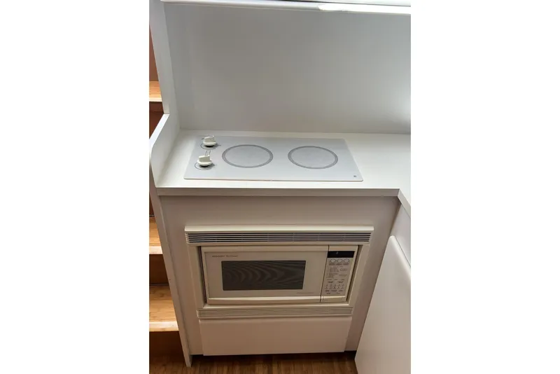Slide: The Image of Compact kitchen area with a built-in microwave and electric cooktop on a 1996 Hatteras 39 Sport Express. - 33