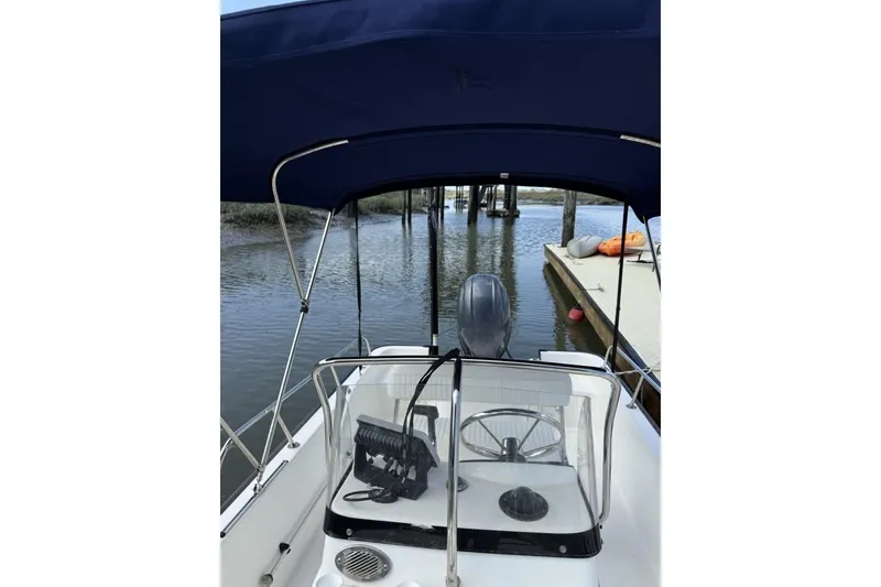 Slide: The Image of 2016 Boston Whaler 170 Montauk boat with canopy, docked by a calm waterway. - 10