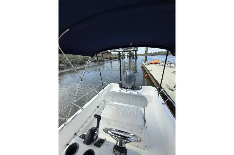 Slide: The Image of 2016 Boston Whaler 170 Montauk boat interior with canopy, docked by a calm river. - 11