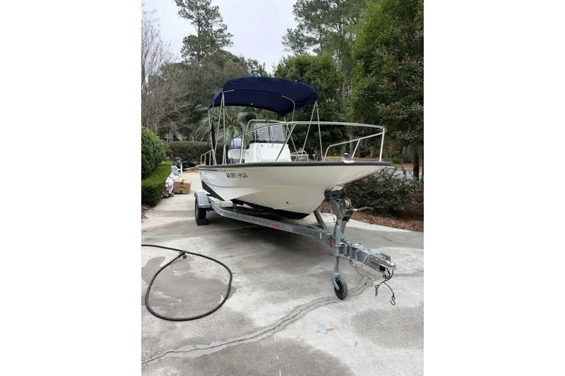 Slide: The Image of 2016 Boston Whaler 170 Montauk boat on trailer, parked in a driveway with trees in background. - 2