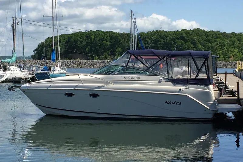The Image of 2003 Rinker Fiesta Vee 270 boat docked in a marina with scenic background. - 1
