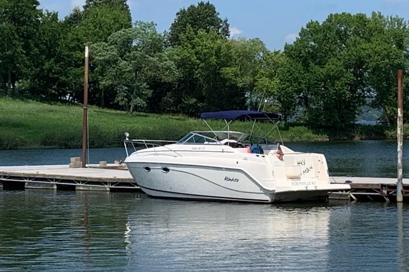 Slide: The Image of 2003 Rinker Fiesta Vee 270 boat docked on a serene lake with lush greenery. - 1