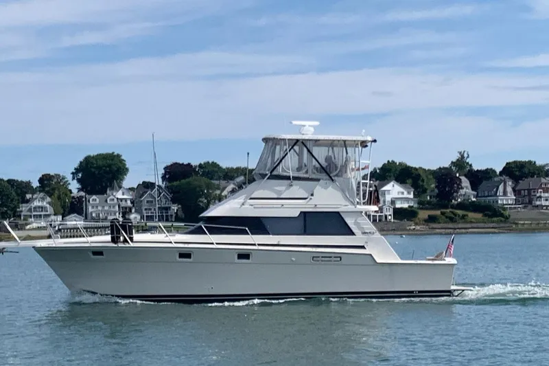 The Image of 1987 Luhrs 40 Convertible yacht cruising near coastal homes on a sunny day. - 0