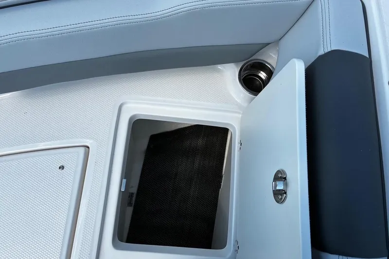 Slide: The Image of 2025 Robalo R207 Dual Console boat storage compartment with open hatch and cup holder. - 14