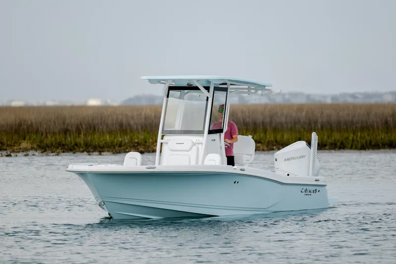 Slide: The Image of 2026 Caymas 24 HB boat cruising on calm water with scenic marshland backdrop. - 2