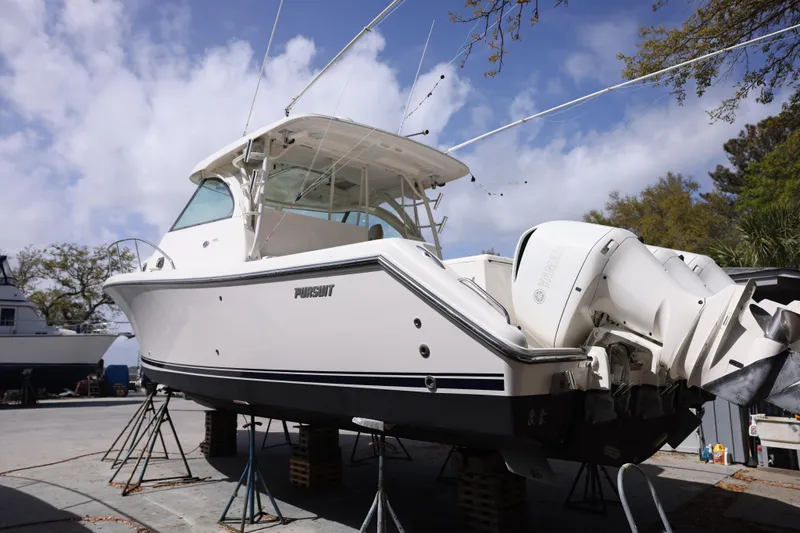 Slide: The Image of 2015 Pursuit OS 385 Offshore boat on stands, viewed from the rear, under a cloudy sky. - 7