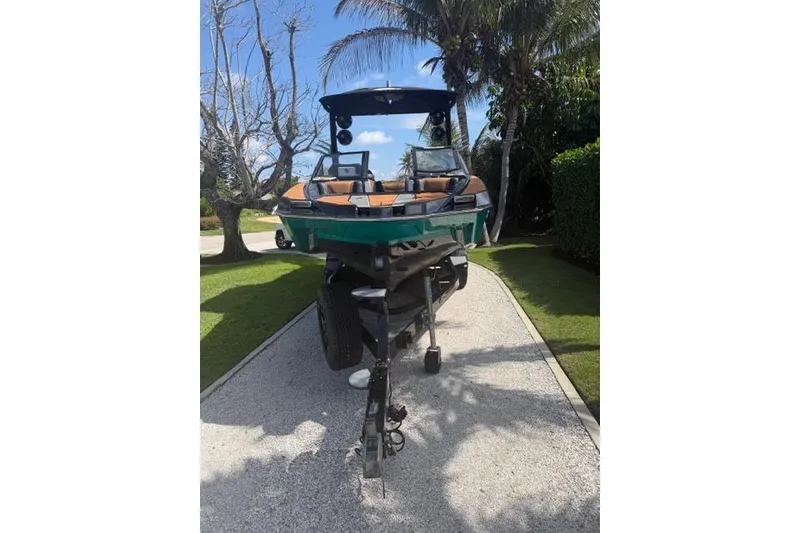 Slide: The Image of 2021 Malibu M240 boat on trailer, parked on a sunny driveway. - 12