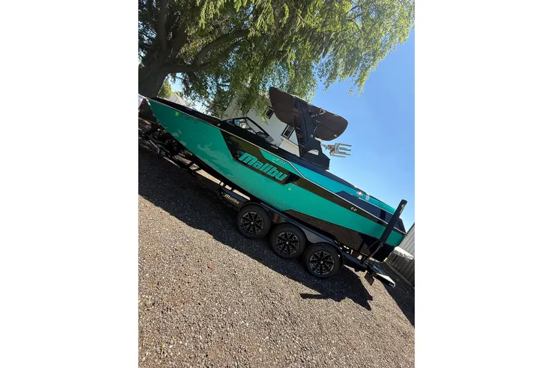 Slide: The Image of 2021 Malibu M240 boat on trailer, parked under a tree, showcasing sleek design. - 14