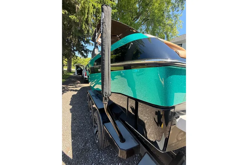 Slide: The Image of 2021 Malibu M240 boat on trailer, vibrant teal color, parked outdoors. - 15