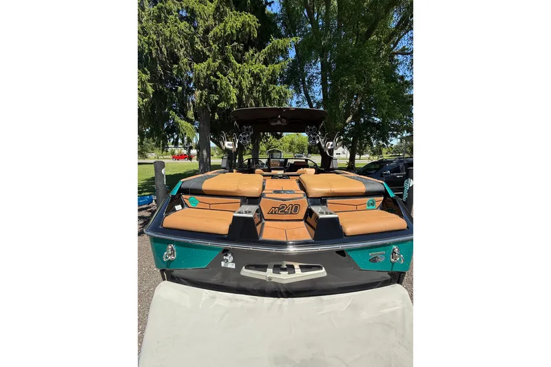 Slide: The Image of 2021 Malibu M240 boat with tan seating, parked outdoors near trees. - 16
