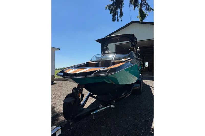 Slide: The Image of 2021 Malibu M240 boat on trailer, parked outside a garage under clear blue sky. - 19