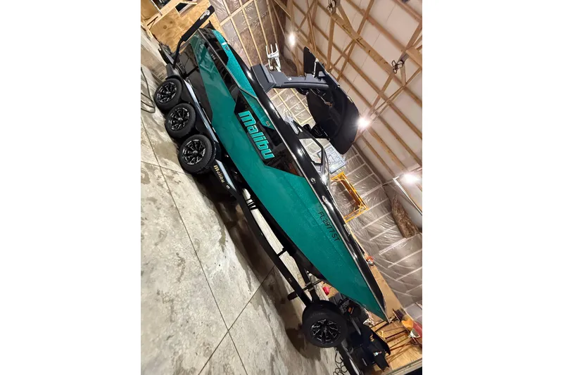 Slide: The Image of 2021 Malibu M240 boat in a garage, teal and black design, on a trailer. - 20